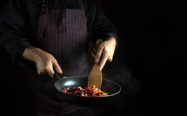 Şef kızartma tavasında sebze hazırlar. Lezzetli vejetaryen yemekleri. Siyah arkaplanda reklam alanı