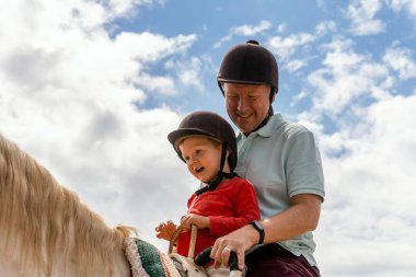 Baba ve oğul otlakta ata binerken eğleniyorlar.