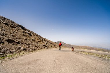Yokuş aşağı hızla giden profesyonel bisikletçi ve Sierra Nevada dağları, Endülüs, İspanya 'da yokuş yukarı mücadele eden küçük motorcu çocuk.