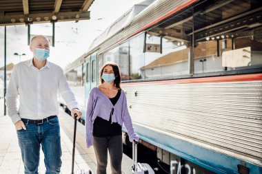 Trenin yanındaki platformda bavul ve maskeli turistler, Portekiz