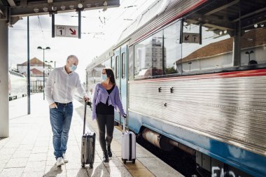 Trenin yanındaki platformda bavul ve maskeli turistler, Portekiz