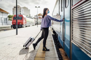 Bavulu ve maskesi olan bir turist trene binmek istiyor, Portekiz