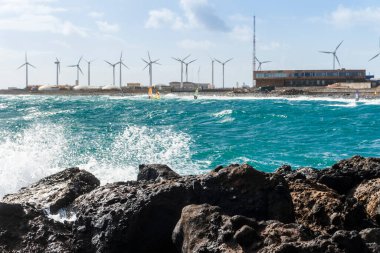 Water splashing on the rocks with windsurfers and windmills in the background, Pozo Izquierdo, Gran Canaria, Spain