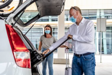 Havaalanında koruyucu maskeli bir yolcuya yardım eden bir taksi ya da Uber sürücüsü.
