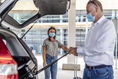Havaalanında koruyucu maskeli bir yolcuya yardım eden bir taksi ya da Uber sürücüsü.