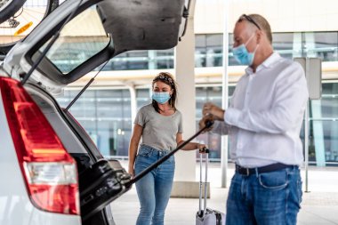Havaalanında koruyucu maskeli bir yolcuya yardım eden bir taksi ya da Uber sürücüsü.