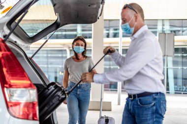 Havaalanında koruyucu maskeli bir yolcuya yardım eden bir taksi ya da Uber sürücüsü.