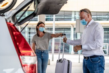 Havaalanında koruyucu maskeli bir yolcuya yardım eden bir taksi ya da Uber sürücüsü.