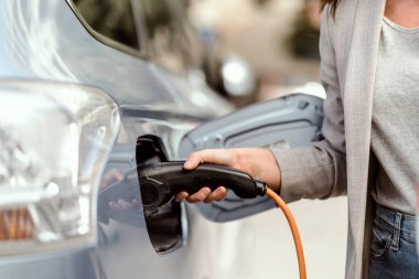 Şehir ortamında elektrikli araba şarj eden genç bir kadın