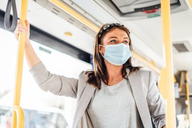 Kamu otobüsünün yanından geçerken koruyucu maske takan genç bir kadın.