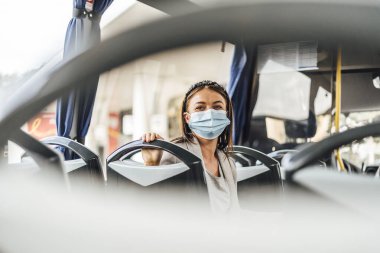 Kamu otobüsünün yanından geçerken koruyucu maske takan genç bir kadın.