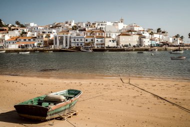 Cityscape of whitewashed town with a traditional wooden fishing boat on the beach in the foreground, Ferragudo, Algarve, Portugal