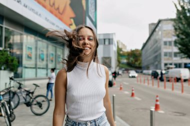 Parlak tatilli neşeli bayan şehrin arka planında mutluluğunu ifade ediyor. Şehvetli esmer kadın manken sokakta gülüyor..