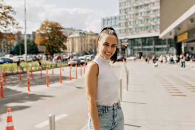 Kendine güvenen, kendine güvenen, saçları ve modası olan, günlük tişört ve kot pantolon giyen, Avrupa 'nın sokaklarında gün ışığında yürüyen, kendine güvenen bir kadın.