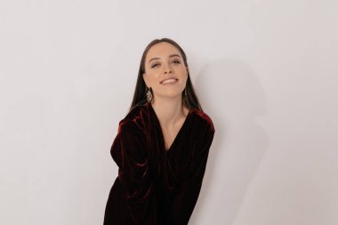 Şık giyinmiş, altın kazançları olan çekici bir kadın izole edilmiş arka planda kameraya gülümsüyor. Sakin, mutlu esmer kadın kameraya bakıyor ve gülüyor. 