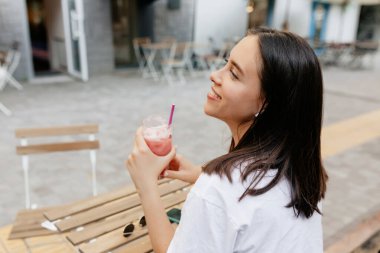 Close up portrait from back of adorable woman with brown hair drinking smoothie in open air terrace in warm day