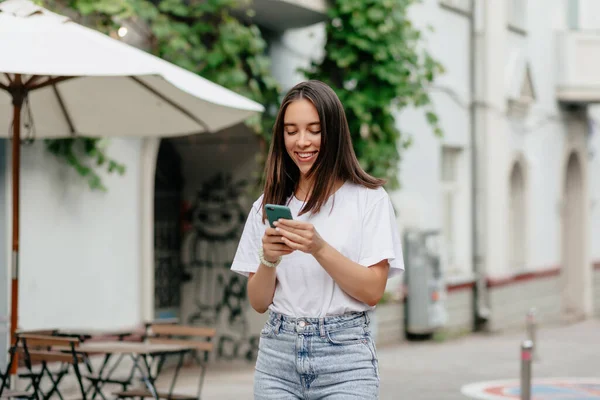 Adorable lovely woman with smile using smartphone while walking on the city in warm good day — Photo