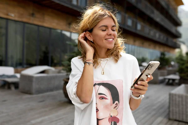 Wanita Pirang Yang Cantik Memegang Smartphone Dan Menyentuh Rambutnya Pagi — Stok Foto