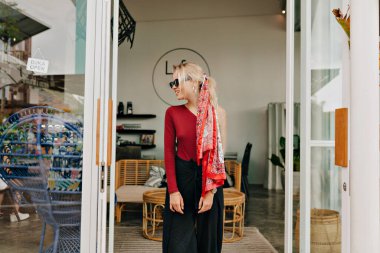 Sarı saçlı, kiraz rengi süveter giyen, siyah pantolonlu, modern moda kafeteryasında gülümseyen güzel bir kadın.