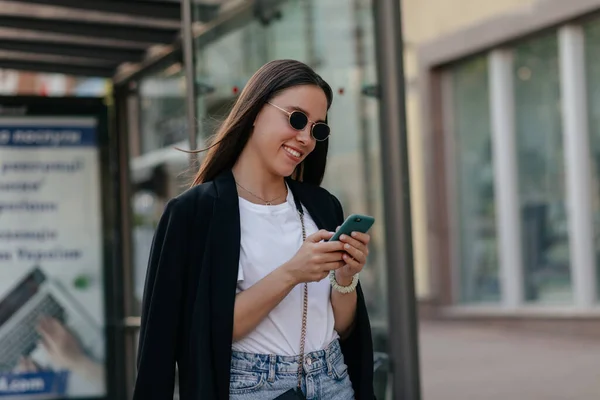 Happy Tersenyum Wanita Muda Berkacamata Hitam Menggulung Smartphone Dan Berjalan — Stok Foto