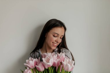 Pembe çiçekli güzel genç bayanın portresi mutlu bir gülümseme ve kapalı gözlerle izole bir arkaplanda poz veriyor. Yüksek kalite fotoğraf