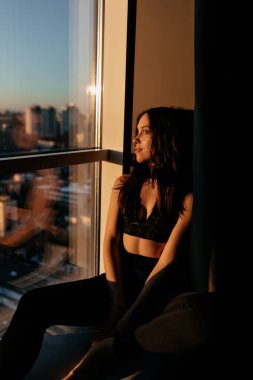 Spor üniformalı güzel bir kadının uzun boylu portresi sabah yogasından sonra dinleniyor. Kadın sabah güneş ışığında pencerenin yanında oturuyor. Yüksek kalite fotoğraf