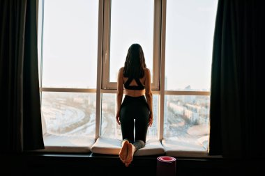 Formalı, siyah saçlı, formalı, formalı genç bir bayanın tam teşekküllü fotoğrafı şehir manzaralı pencerenin yanında sabah yogası yapıyor. Yüksek kalite fotoğraf