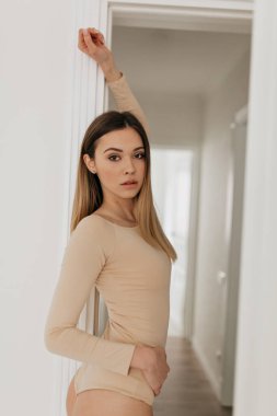 Pencerenin önündeki aydınlık odada güzel bir kızın portresi. Bej giysili muhteşem zarif bayan elini kaldırıp kameraya bakıyor.