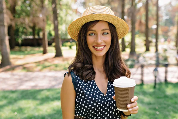 Manis tersenyum wanita cantik dengan rambut gelap dan senyum indah memegang cangkir dengan kopi dan melihat kamera — Stok Foto