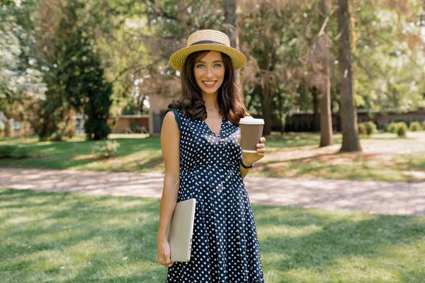 꽤 매력적 인 아가씨가 여름옷을 입고 모자를 쓰고 커피를 마시며 노트북 과 컵을 들고 있습니다 — 스톡 사진