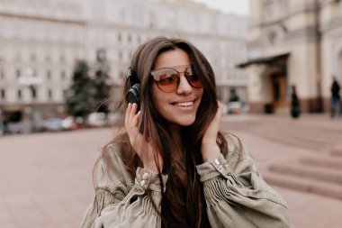 Avrupalı siyah saçlı, kahverengi gözlükler takan ve kulaklıkla müzik dinleyen güzel bir kadının yakın portresi gülümsüyor ve şehirde akşam yemeği yiyor.. 