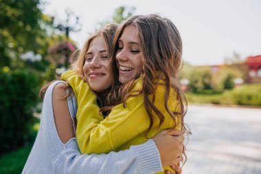 Koyu saçlı, kız kardeşini kucaklayan, gülümseyen ve gözleri kapalı bir kadını cezbediyor. İyi giyimli bayan arkadaşlarının açık havada çekimleri var.