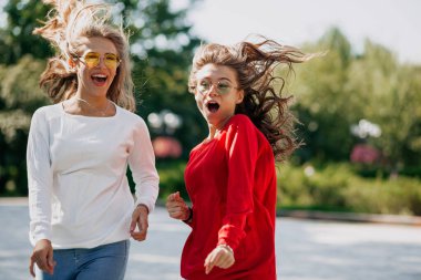 Heyecanlı iki güzel kız dışarıda gülüyor ve dans ediyor. Moda gözlükleri ve parlak kazaklar takıyorlar ve uçan saçlarla poz veriyorlar. Yüksek kalite fotoğraf