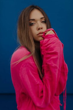 Pembe bluzlu esmer güzel kadının şık portresi kameraya poz veriyor ve mavi duvarın üzerinden yüzüne dokunuyor. Yüksek kalite fotoğraf