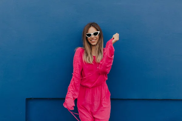 迷人的漂亮女士 深色的发型 穿着粉色亮丽的衣服 在蓝色的背景墙上微笑和跳舞 高质量的照片 — 图库照片