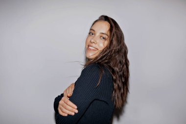 Stylish charming european girl with wavy long hair wearing black polo is posing at camera with arms crossed on his chest over isolated background. High quality photo