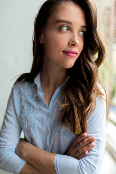 Uzun dalgalı saçlı romantik güzel bir bayanın yakın portresi pencereye bakıyor ve mutlu bir gülümsemeyle pencereye bakıyor. Güzel kız, romantik manzaralı pencerenin kenarında dinleniyor.