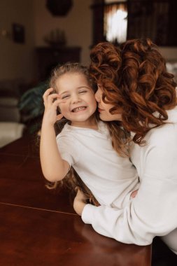 Heyecanlı küçük sevimli kız evde eğleniyor ve annesine sarılıyor. Genç kadın küçük kızıyla vakit geçiriyor. Yüksek kalite fotoğraf