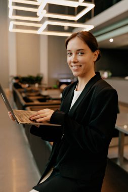 Şirin, güzel bir işçi, mutlu bir gülümsemeyle dizüstü bilgisayarla modern ofisteki kameraya bakıyor. Kablosuz kulaklıklı kız, video aracılığıyla gülümseyerek iletişim kuruyor.