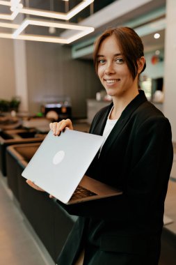 Çalışmak için dizüstü bilgisayar kullanan çekici bir kadın işçi. Ofiste içi aydınlık bir şekilde oturuyor. Ofisin yanında gülümseyerek poz veren büyüleyici bir kadın portresi..