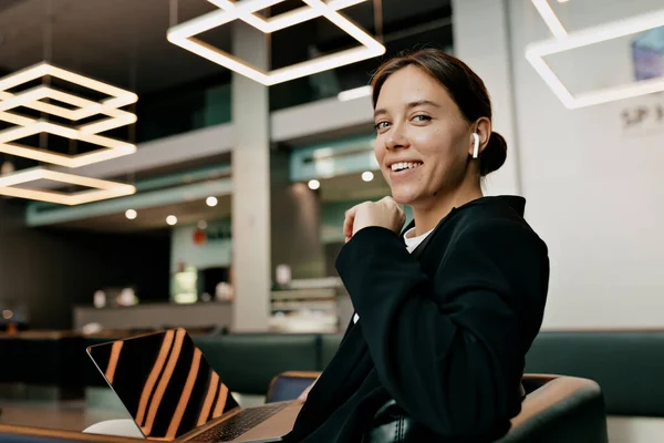 Kapalı alanda siyah saçlı sevimli bir bayanın portresi kulaklıklı koyu renk bir takım elbise giyiyor modern ofiste çalışırken kameraya mutlu bir gülümsemeyle bakıyor.