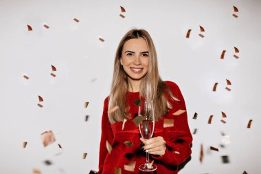 Açık renk saçlı ve makyajlı sevimli bir bayan konfeti altında mutlu bir gülümsemeyle kırmızı süveter içinde gülümsüyor. Yüksek kalite fotoğraf