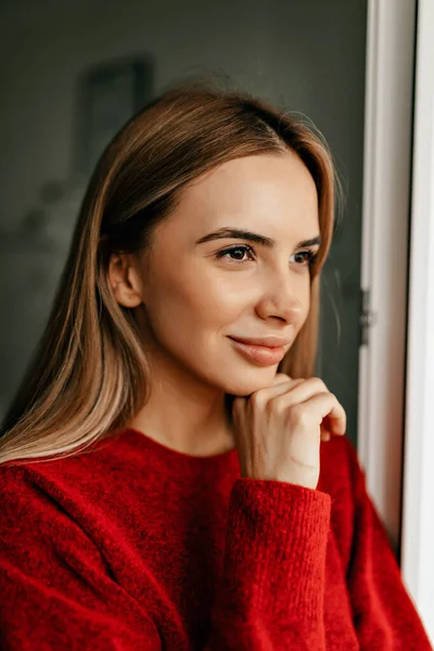 Kapalı mekanda, arka planda tatlı tatlı gülümseyen çekici bir kız. Uzun açık renk saçı ve geniş gülüşü olan çekici bir kadın..