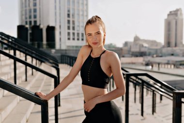 Spor giyim sektöründe şık, çekici ve formda bir kadın spor salonunda güneşli bir ortamda kameraya poz veriyor. Yüksek kalite fotoğraf