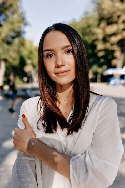 Gömlek açık havada gülümserken oldukça çekici bir genç kız. Mutlu, güzel, siyah saçlı kadın güneşli bir günde parkta yürüyor.