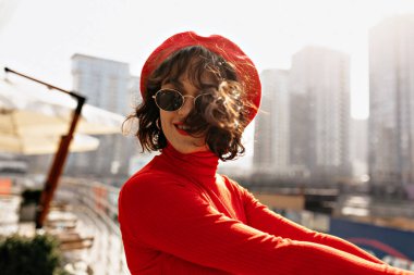 Kısa saçlı, kısa saçlı, şapka takan ve güneş gözlüklü hoş bir bayanın yakın plan portresi kameraya poz veriyor ve gülümsüyor. Yüksek kalite fotoğraf