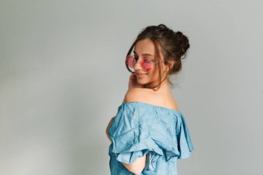 Çekilmiş arka planda kameraya gülümseyen sevimli bayanın yakın çekimi. Kahverengi saçları ve çıplak makyajı var. Güneş gözlükleri yüzdeki gözleri kapatır..