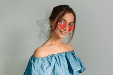 Çekici Avrupalı, koyu saçlı, yuvarlak gözlüklü ve mavi gömlekli gülen kız, izole edilmiş arka planda sevimli bir gülümsemeyle kameraya poz veriyor. Yüksek kalite fotoğraf