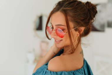 Güneş ışığı altında gülümseyen yuvarlak gözlüklü, bronz tenli sevimli bir kızın portresini yakından çek. 