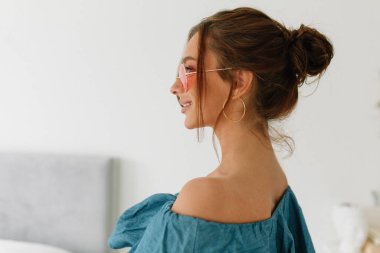 Siyah saçlı, mavi tişörtlü, pembe gözlüklü, gülümseyen ve dimdik duran sevimli bir bayanın yakın plan fotoğrafını çek. Yüksek kalite fotoğraf